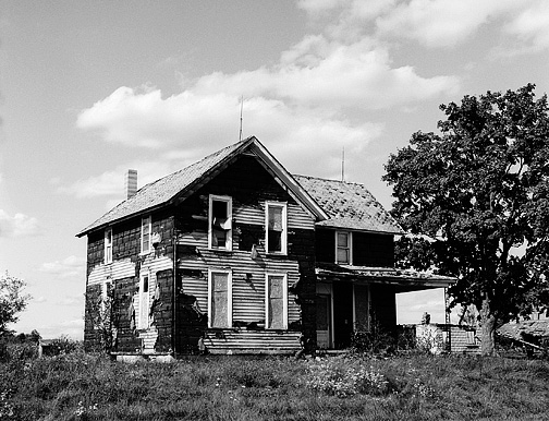 An abandoned farmhouse in Allen County, Indiana near Fort Wayne International Airport. The original siding is visible under tar paper that covered it. There are lightning rods on the roof.